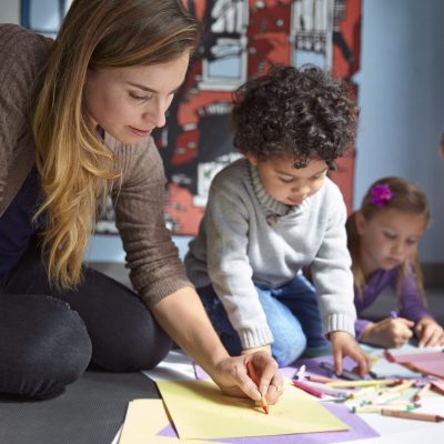 Teacher Drawing On Papers With Students At Preschool